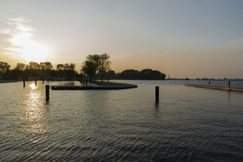Coucher de soleil sur l'eau à Houseboat Aqua Dolce à Friesland, Pays-Bas, avec arbres et quais visibles.