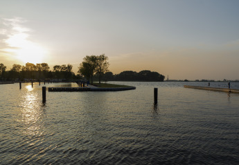 Tramonto visto dall’Houseboat Aqua Dolce a Friesland, Paesi Bassi, con alberi e pontili visibili sull'acqua.