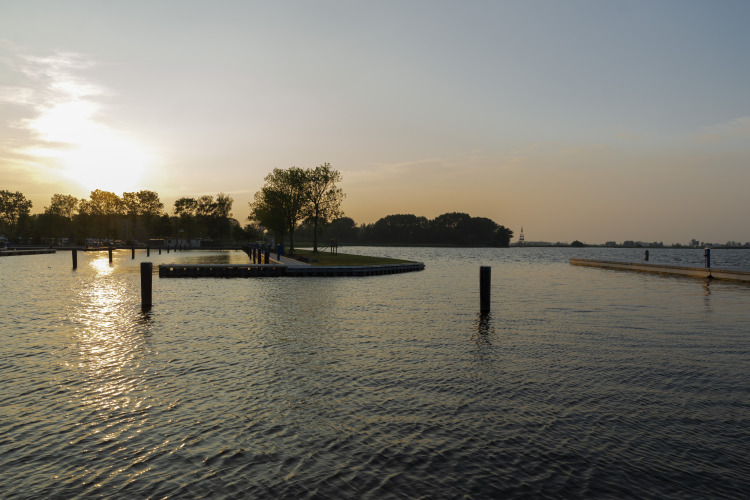 Sunset view over the water at Houseboat Aqua Dolce in Friesland, Netherlands, with trees and docks visible.