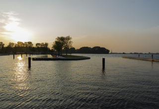 Zonsondergang aan het water bij Houseboat Aqua Dolce in Friesland, Nederland, met bomen en steigers.