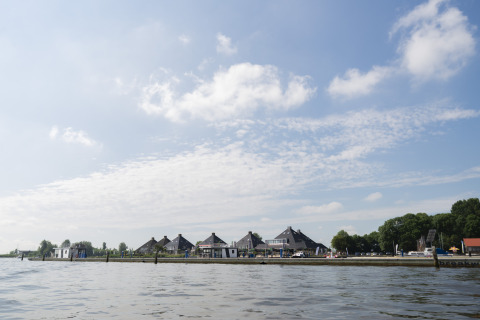 Foto genomen vanaf een woonboot met zicht op huizen aan het water en een blauwe lucht met wolken.