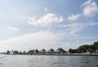 Foto genomen vanaf een woonboot met zicht op huizen aan het water en een blauwe lucht met wolken.
