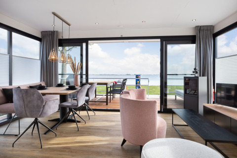 Salón moderno de casa flotante con vistas al lago, mesa de comedor y sillas elegantes en ambiente luminoso.