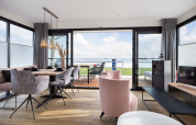 Salón moderno de casa flotante con vistas al lago, mesa de comedor y sillas elegantes en ambiente luminoso.