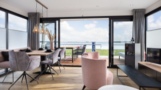 Salón moderno de casa flotante con vistas al lago, mesa de comedor y sillas elegantes en ambiente luminoso.