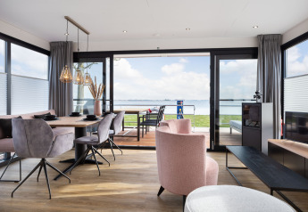 Salon moderne sur une péniche avec vue sur le lac, table à manger et fauteuils élégants dans un décor lumineux.