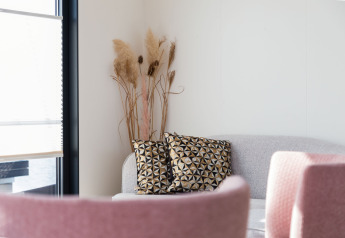 Rincón luminoso de salón en una casa flotante con sofá gris, cojines geométricos y sillas rosas.