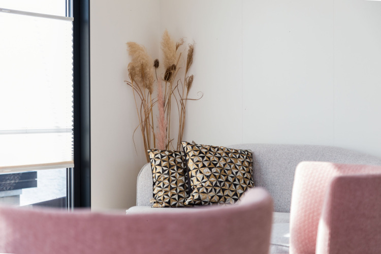 Bright houseboat living area with a gray sofa, geometric cushions, pink chairs, and dried grass decor.