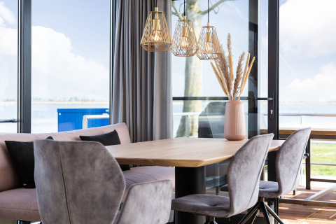 Comedor moderno en una casa flotante con grandes ventanales, vista al lago y decoración elegante en Friesland.