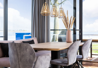 Zona pranzo moderna su una casa galleggiante con grandi finestre, vista lago e arredo elegante in Friesland.