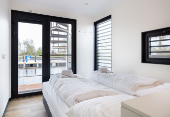 Chambre lumineuse sur la péniche 'de Valreep' avec deux lits simples et vue sur l’eau à Friesland, Pays-Bas.