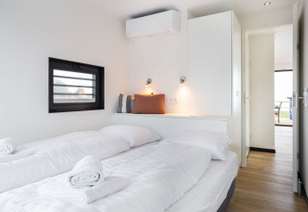 Moderne slaapkamer op woonboot 'de Valreep' met witte bedden, raam en minimalistische inrichting in Friesland.