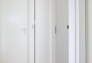 Interior hallway of Houseboat 'de Valreep' featuring white doors and light wooden floors in Friesland, NL.