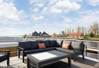 Terrazza della houseboat 'de Valreep' con divano e vista sul porto turistico in Friesland, Paesi Bassi.