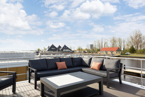 Terras van houseboat 'de Valreep' met zithoek en zicht op jachthaven in Friesland, Nederland.