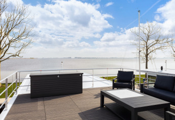 Terraza de una casa flotante con asientos modernos y vista al lago en Welcome In - Friesland, Países Bajos.