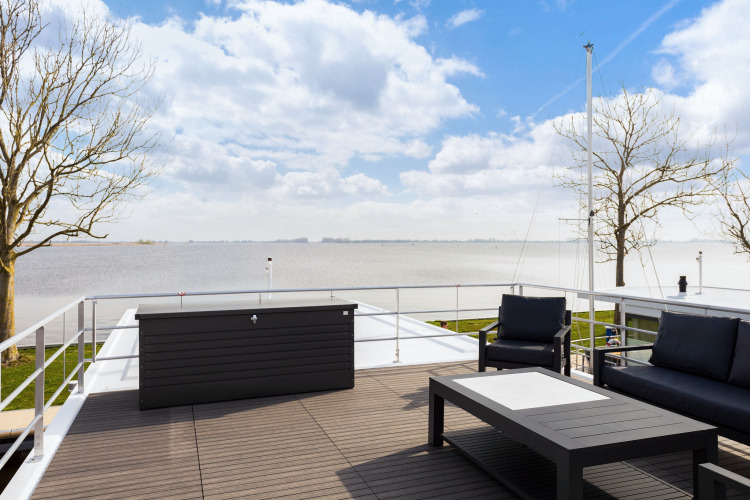 Terraza de una casa flotante con asientos modernos y vista al lago en Welcome In - Friesland, Países Bajos.