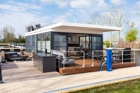 Modernes Hausboot mit Terrasse am Steg, umgeben von Natur im Friesland, Niederlande.