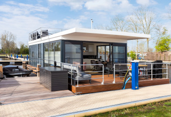 Péniche moderne avec grande terrasse amarrée à un quai, située en Frise, aux Pays-Bas.