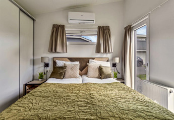Chambre à la Natuurlodge Wellness avec lit double, couvre-lit vert, fenêtre et décoration moderne.