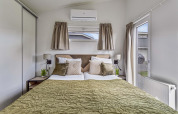 Slaapkamer in Natuurlodge Wellness met dubbel bed, groene sprei, raam en eigentijdse inrichting.