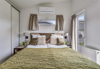 Dormitorio en Natuurlodge Wellness con cama doble, colcha verde, ventana y una decoración moderna.