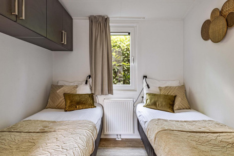 Twee eenpersoonsbedden in een gezellige kamer met raam bij Natuurlodge Wellness, neutrale inrichting.