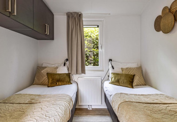 Twin beds in a cozy, compact room at Natuurlodge Wellness with natural light and elegant neutral decor.