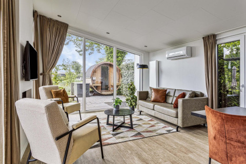 Bright living room at Natuurlodge Wellness with large windows, modern furniture and outdoor spa in the Netherlands.