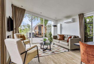 Helles Wohnzimmer der Natuurlodge Wellness mit großen Fenstern, modernen Möbeln und Blick auf Spa draußen.