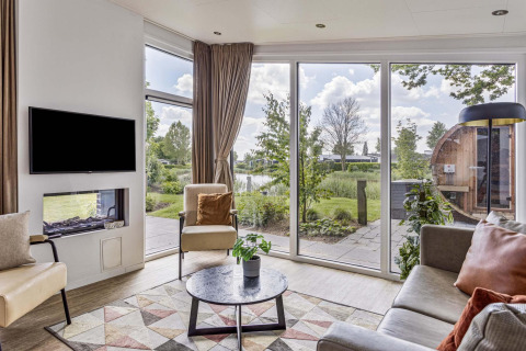 Sala de estar en Natuurlodge Wellness con grandes ventanas, decoración moderna y vista a jardín y spa en Recreatiepark het Esmeer.