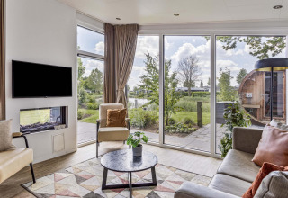 Sala de estar en Natuurlodge Wellness con grandes ventanas, decoración moderna y vista a jardín y spa en Recreatiepark het Esmeer.
