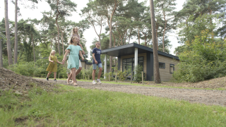 Familie spaziert vor Forest park chalet im Holiday park De Kleine Belties, umgeben von Wäldern in den Niederlanden.