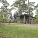 Familia paseando frente al Forest park chalet en Holiday park De Kleine Belties, rodeada de árboles en los Países Bajos.