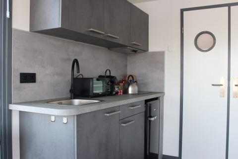 Moderne kitchenette in Marina Parcs Amsterdam met grijze kasten, gootsteen, magnetron en waterkoker.