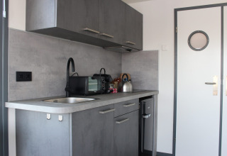 Moderne kitchenette in Marina Parcs Amsterdam met grijze kasten, gootsteen, magnetron en waterkoker.