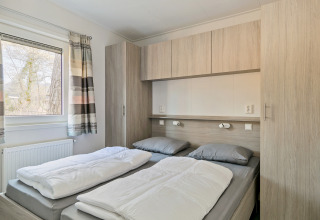 Dormitorio con dos camas individuales, ropa de cama gris, armarios empotrados y ventana en Forest Park Chalet.
