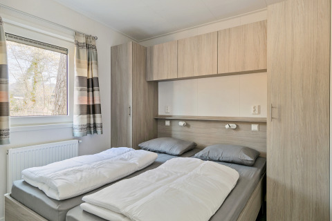 Slaapkamer met twee aparte bedden, grijs beddengoed, inbouwkasten en raam in Forest Park Chalet.