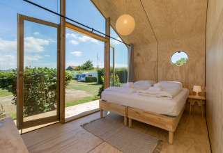 Interior de una acogedora Wikkelhouse en Welcome In - Zeeland con cama doble y puertas de cristal al jardín.