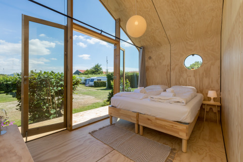 Innenaufnahme eines gemütlichen Wikkelhauses mit Doppelbett und großen Glastüren zum Gartenbereich.