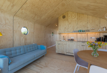 Sala y cocina modernas en un Wikkelhouse con interior de madera clara y ventanas redondas en Zelanda.