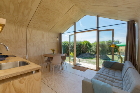 Modern en licht interieur van een Wikkelhouse met grote ramen, bank, eettafel en uitzicht op de tuin buiten.
