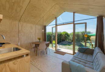 Interno moderno e luminoso di una Wikkelhouse con grandi finestre, divano, tavolo da pranzo e vista sul giardino.
