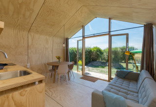 Interior moderno y luminoso de una Wikkelhouse con grandes ventanales, sofá, mesa de comedor y vista al jardín.