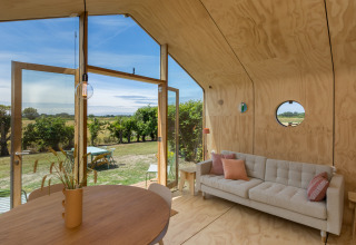 Innenraum eines Wikkelhouse mit heller Einrichtung und Ausblick ins Grüne bei Welcome In - Zeeland, Niederlande.