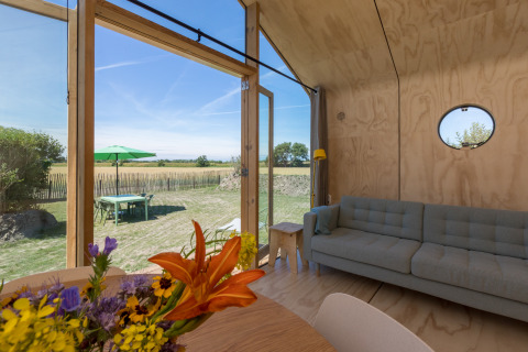 Interior de una Wikkelhouse en Zeeland, Países Bajos, con paredes de madera, sofá y vista al exterior.