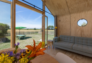 Interior de una Wikkelhouse en Zeeland, Países Bajos, con paredes de madera, sofá y vista al exterior.