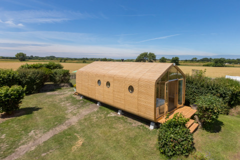 Moderne houten Wikkelhouse omringd door groene velden en struiken in Zeeland, Nederland, overdag buiten gezien.
