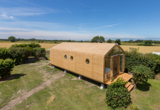 Casa modular Wikkelhouse de madera rodeada de césped y campos verdes en Zeeland, Países Bajos, vista exterior diurna.