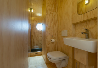 Badkamer met houten wanden, wandtoilet, wastafel en rond raam in een Wikkelhouse in Zeeland, Nederland.